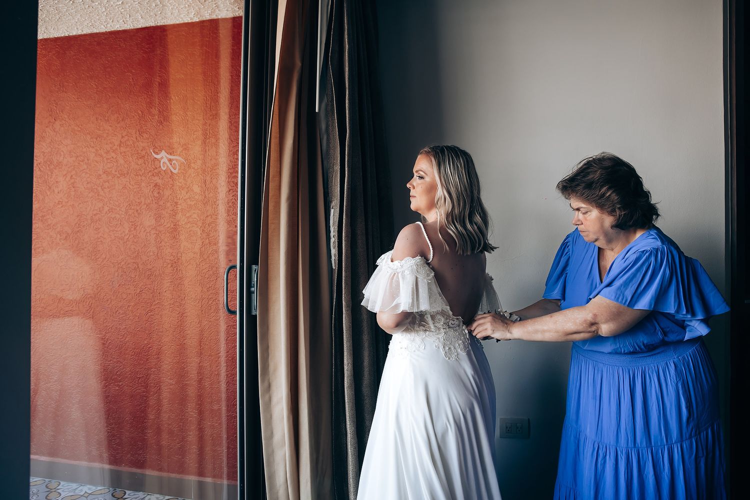 A couple shares a tender moment in a hallway wearing white and blue formal attire.