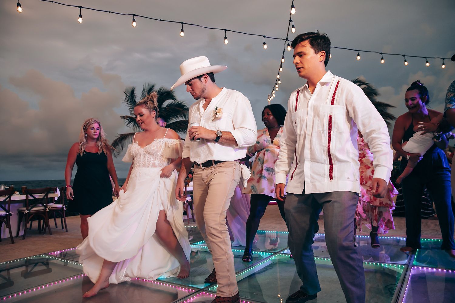 Evening wedding reception with guests dancing under string lights on outdoor patio.
