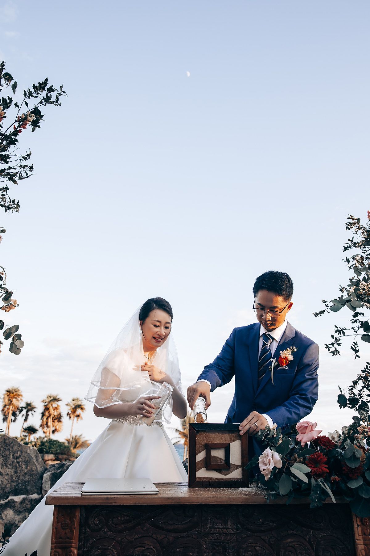 A couple signs documents together at a rustic wooden table during an outdoor wedding ceremony.