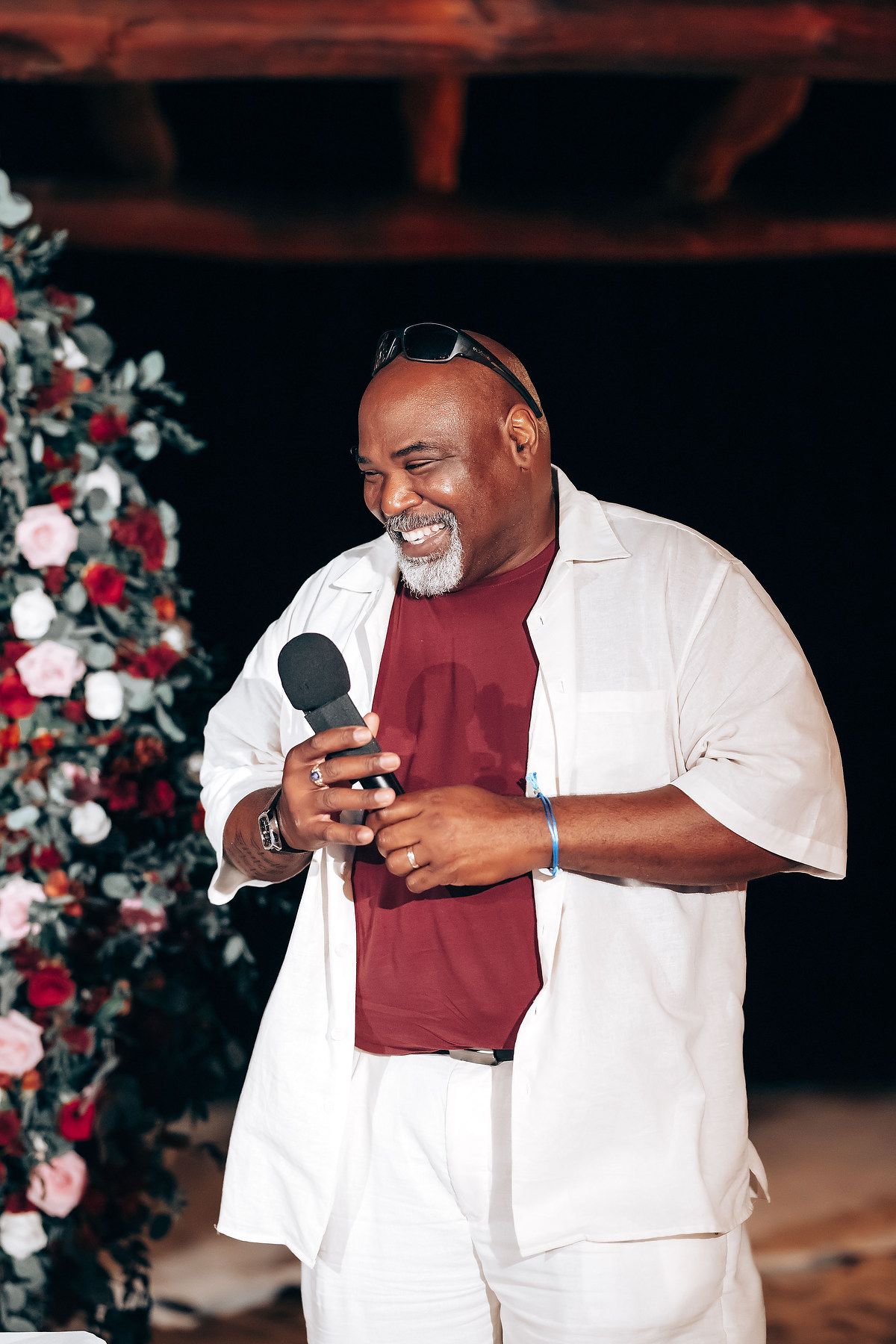 Joyful wedding guest in white suit and burgundy vest laughing during reception celebration.