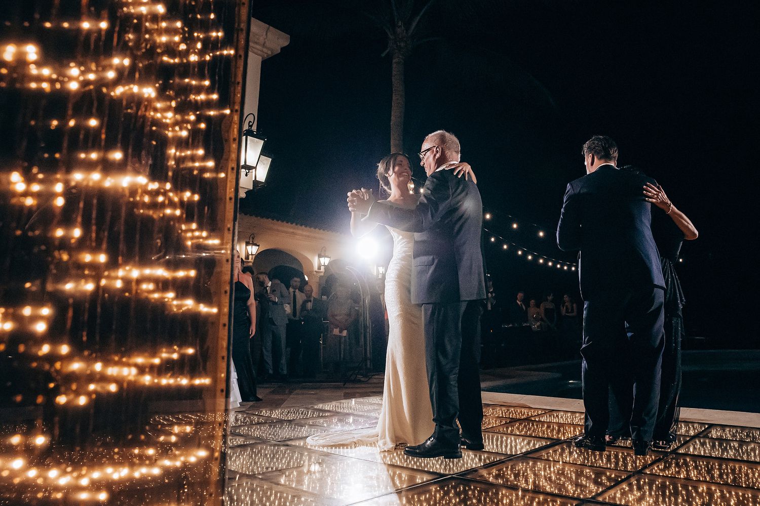 A romantic evening wedding ceremony lit by string lights and spotlights in an outdoor setting.