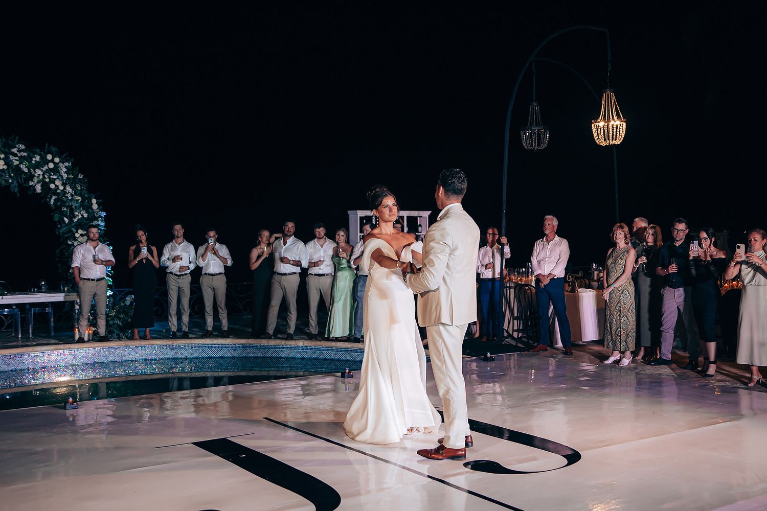 Newlyweds share their first dance together on an illuminated white dance floor at an evening wedding reception.