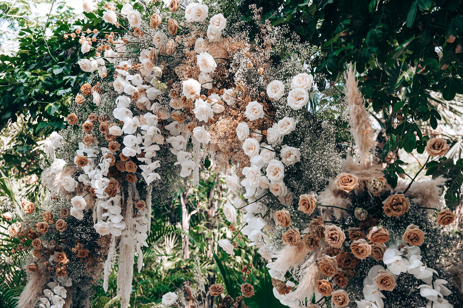 A lush floral installation with white and brown dried flowers cascading from above creates a romantic garden atmosphere.