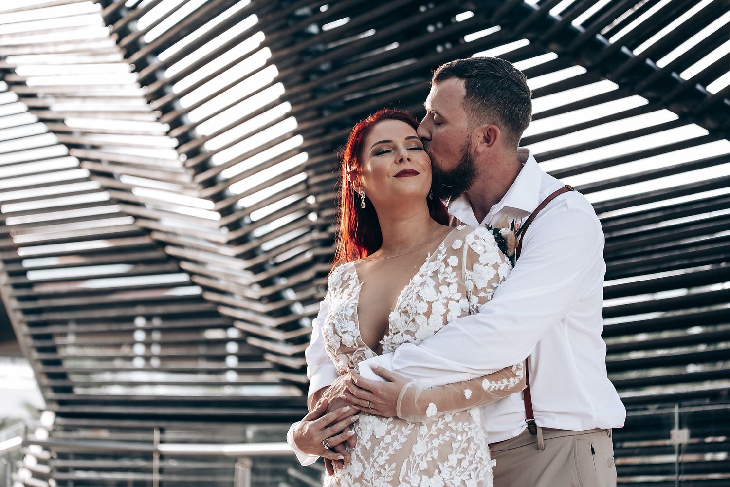 Intimate moment between couple under wooden slat pergola with natural lighting creating dramatic shadows.