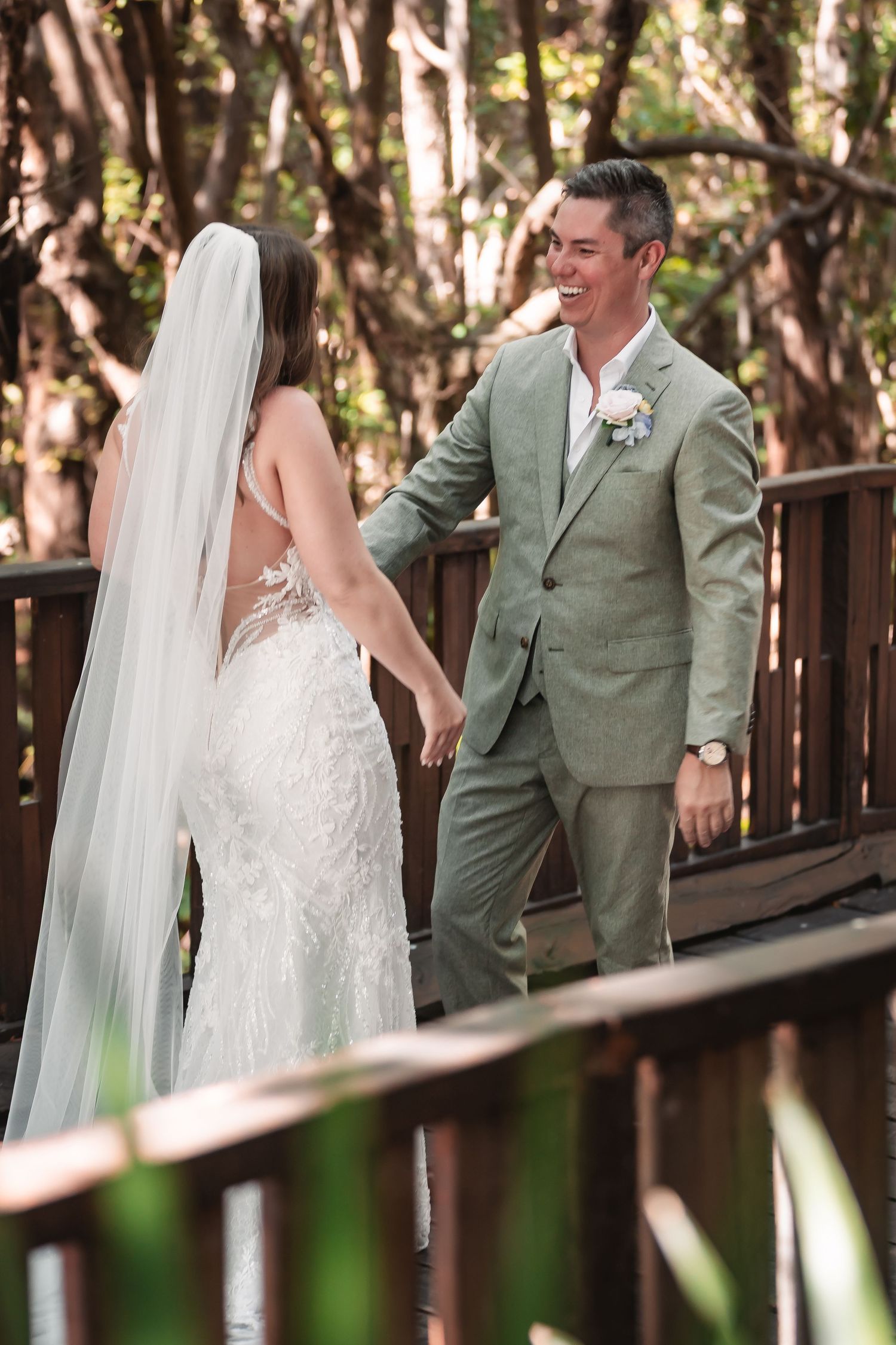 Newlyweds share candid moments along a wooden boardwalk in a tropical setting.