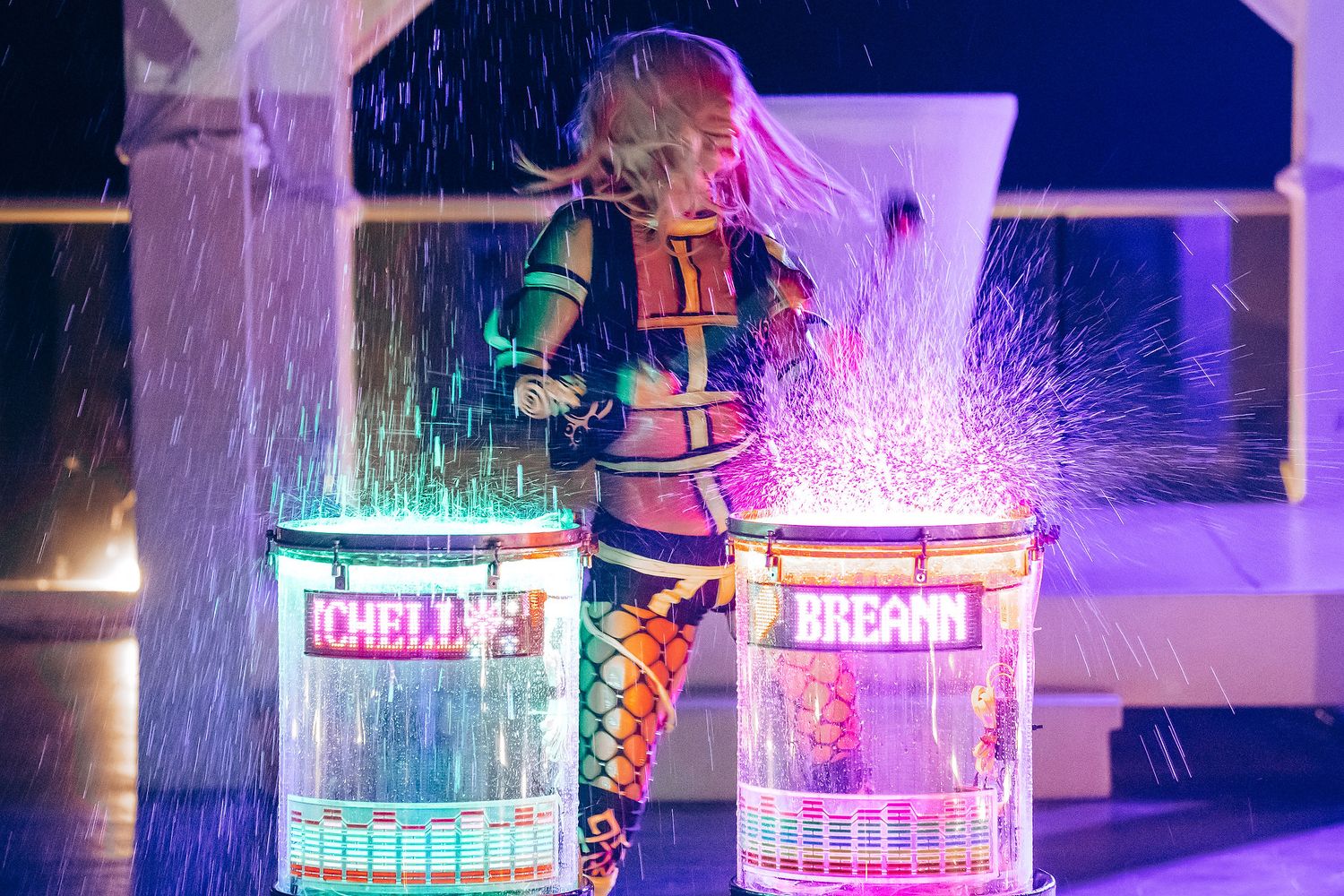 A performer creates sparks while drumming on illuminated drums during a nighttime show.