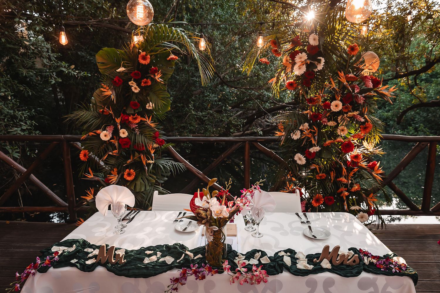 Romantic outdoor wedding table setup with white linens and floral arrangements under glowing string lights at dusk.