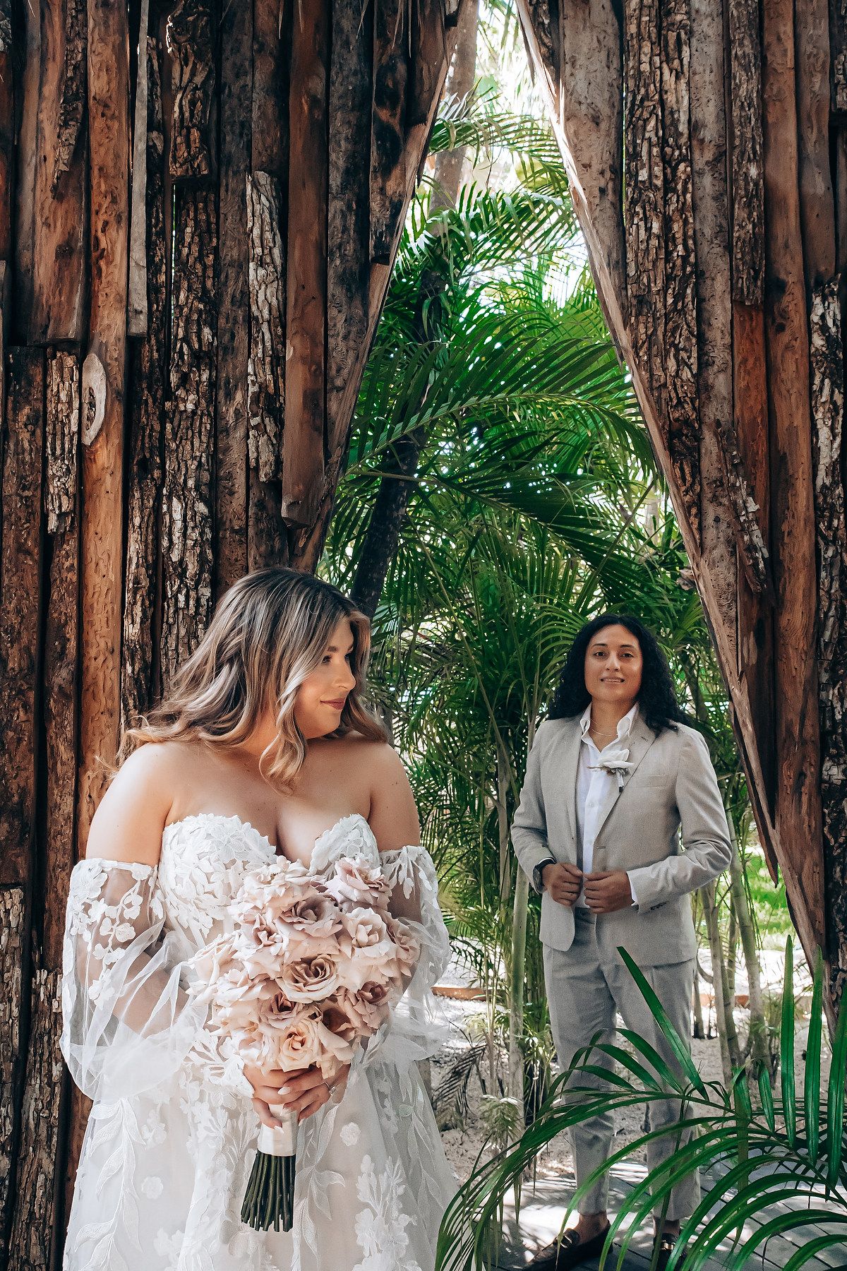 Wedding couple poses against rustic wooden walls surrounded by tropical greenery.
