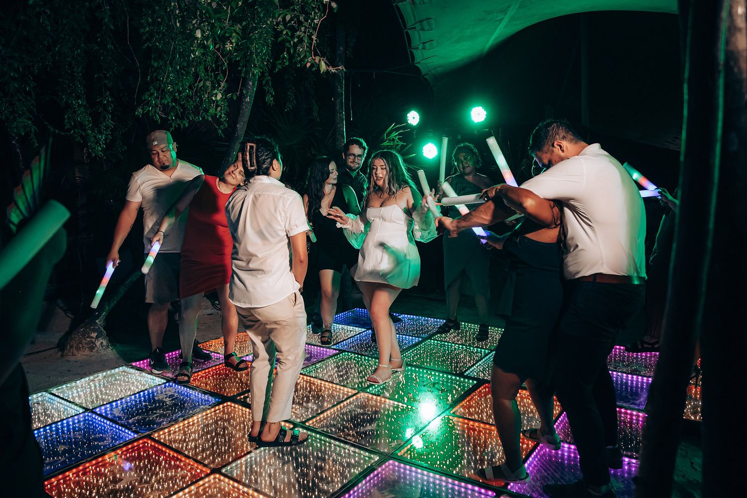 Partygoers dancing on an illuminated floor with green ambient lighting at an outdoor venue.