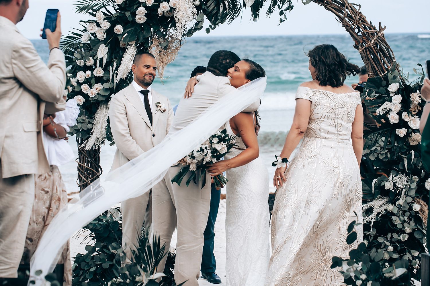 Wedding ceremony under floral arch with ocean backdrop and white roses.