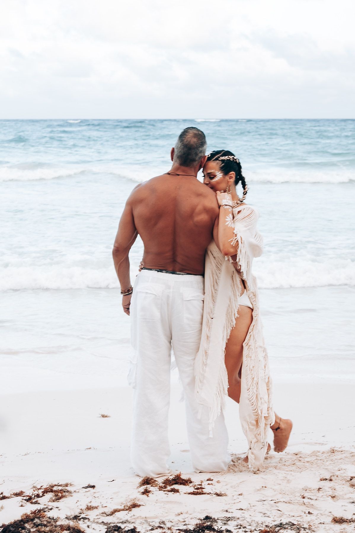 A romantic couple embracing on a sandy beach with waves crashing in the background.