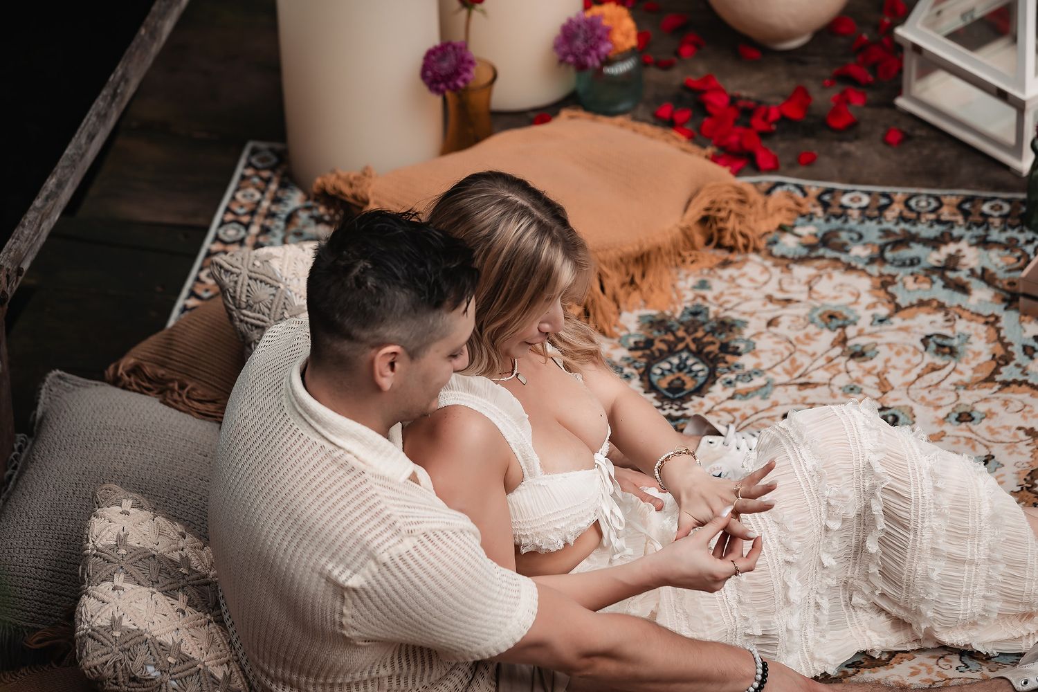 Couple sitting on patterned rug with decorative pillows in intimate setting.