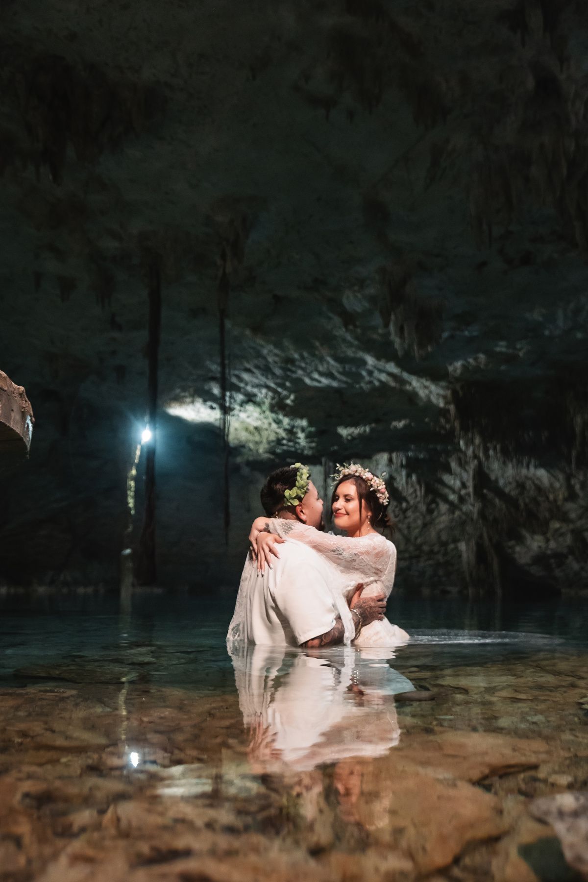 Romantic couple embracing in crystal clear cenote waters during cave photo session.