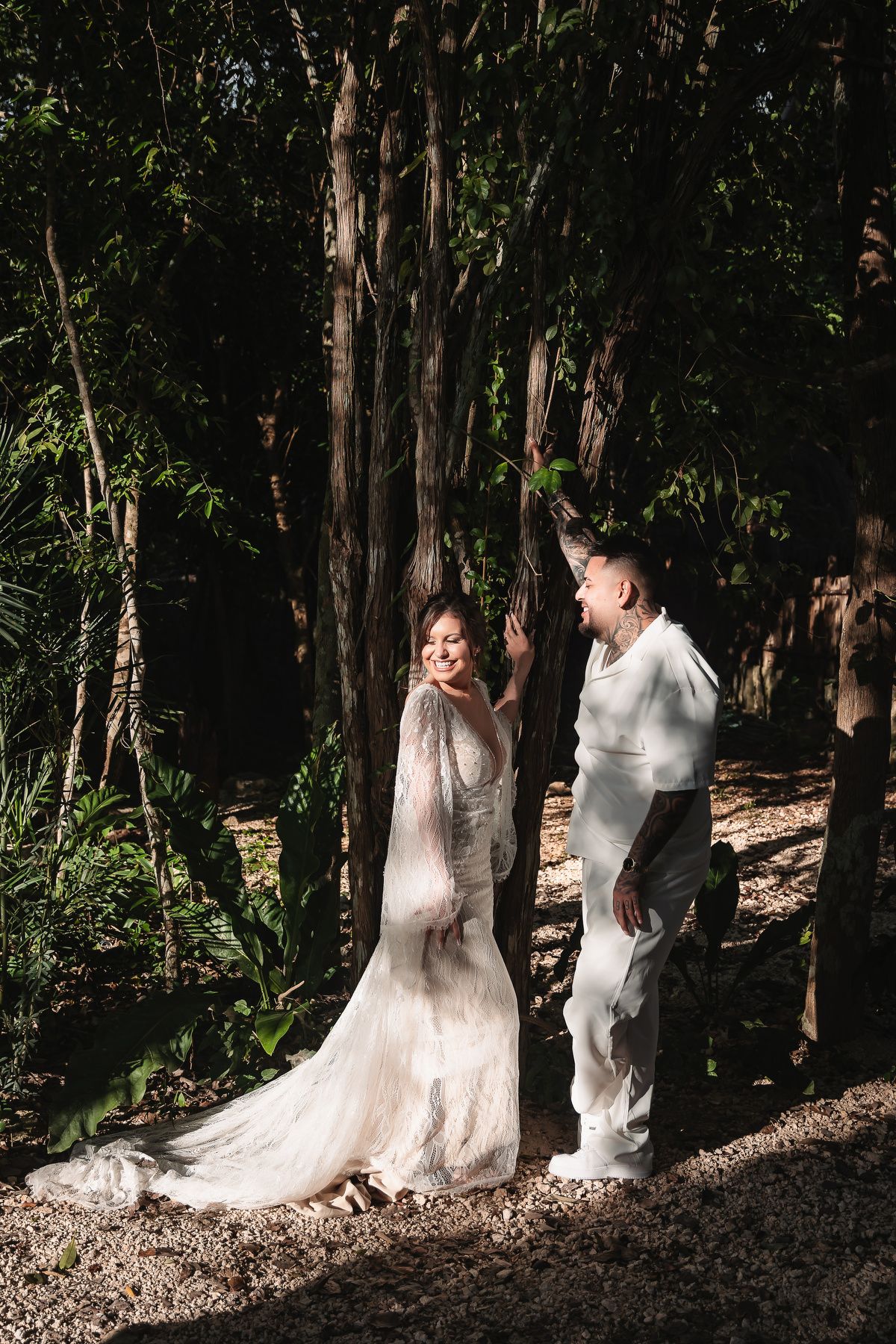 A couple in wedding attire walks together through a sunlit forest path creating a romantic woodland scene.