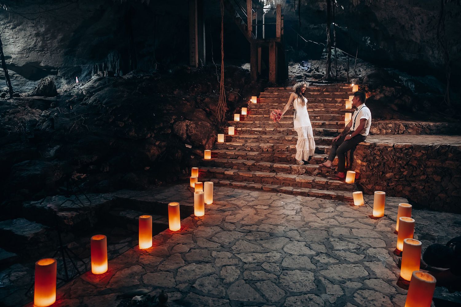 Luminous lanterns line stone steps in a cave as a couple creates a magical wedding moment.