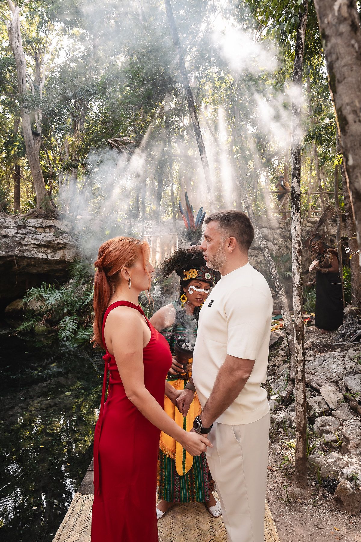 A couple in red and white outfits share a romantic moment in a sunlit forest setting.