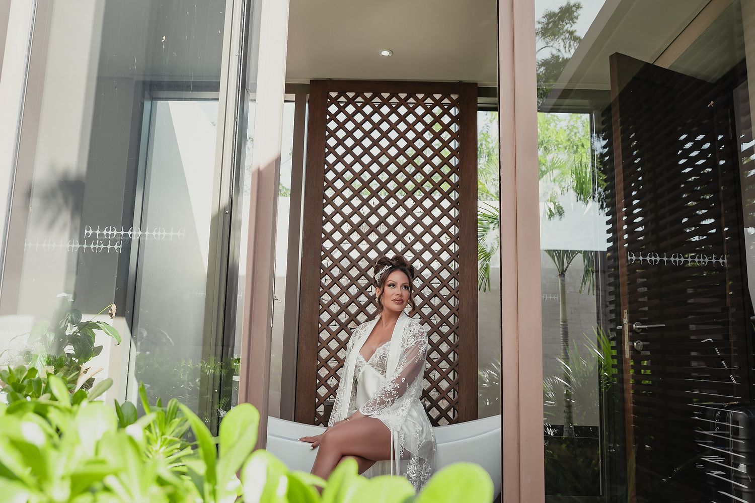 White-robed figure standing on a balcony with tropical greenery and lattice panels in the background.