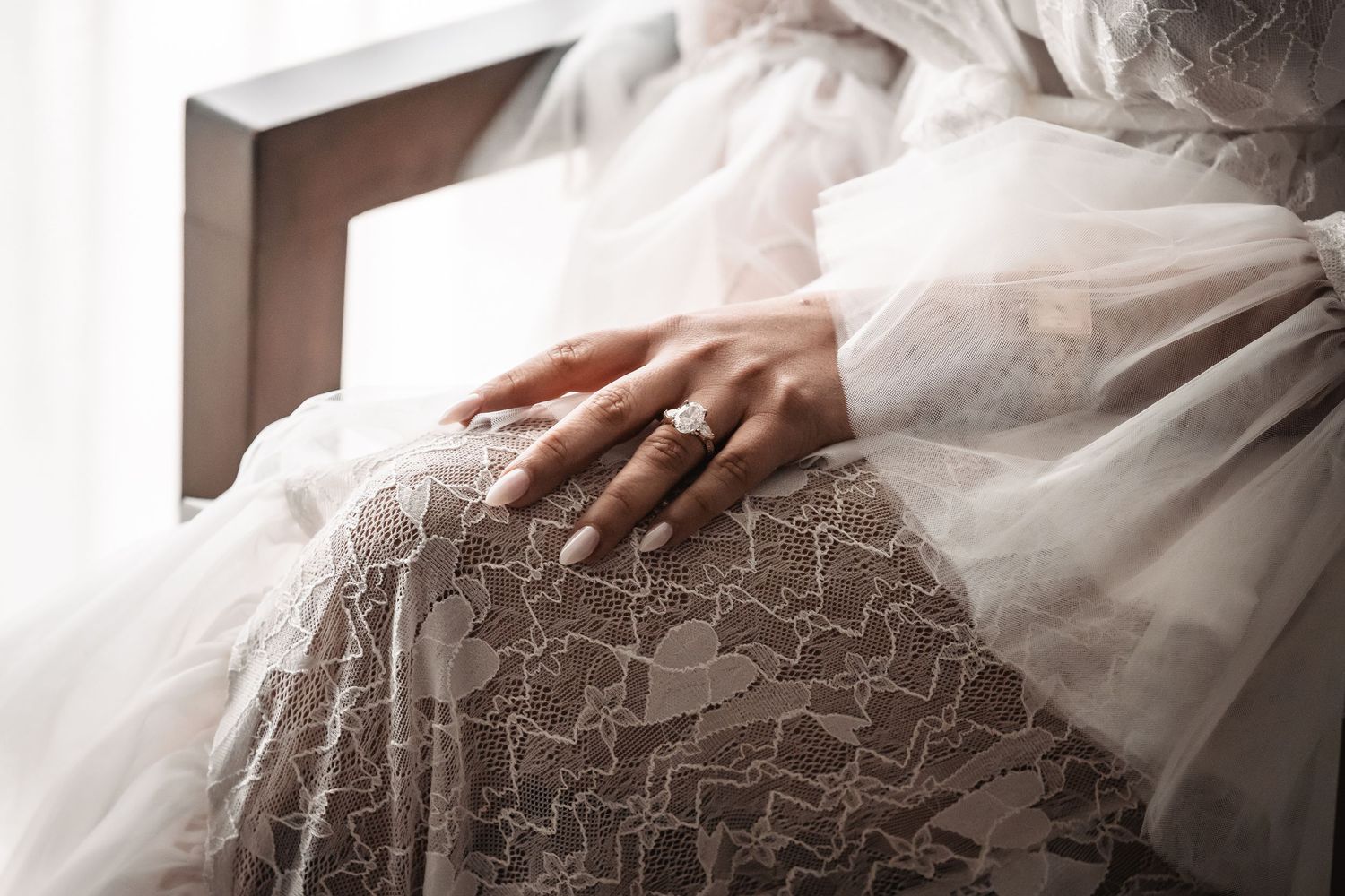 Close up of delicate lace details on a white wedding dress with a hand resting on the fabric.