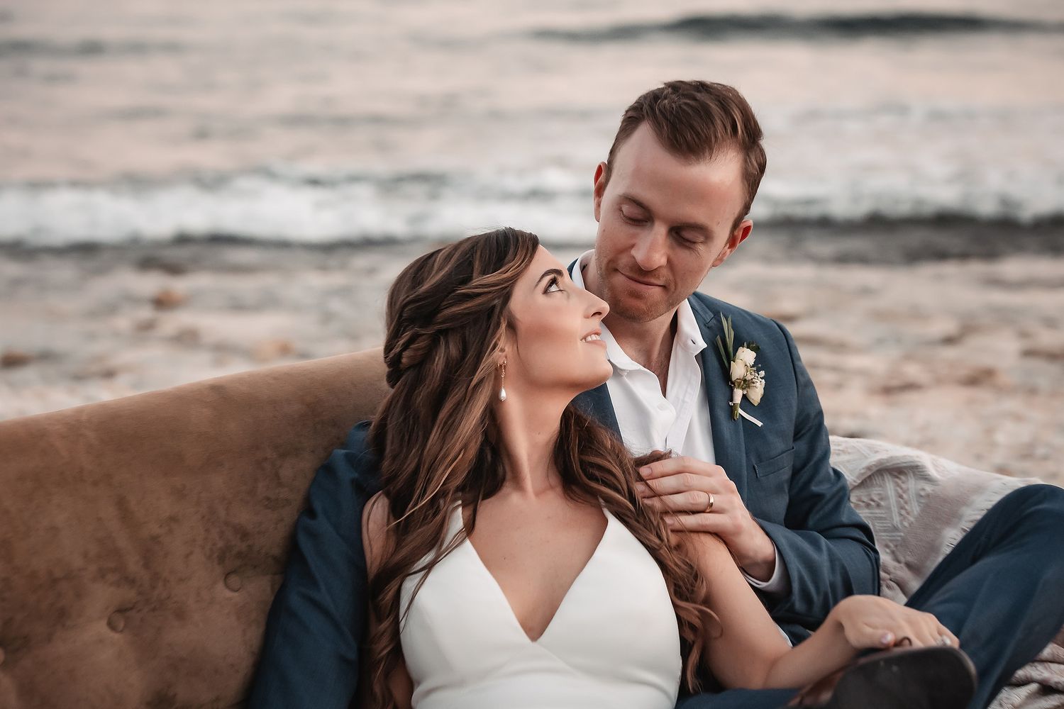 Romantic beachside wedding portraits with couple lounging on vintage leather sofa.