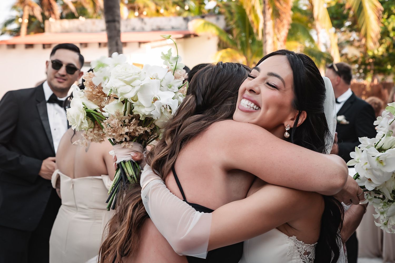 Emotional embrace between wedding attendees with white floral bouquets.