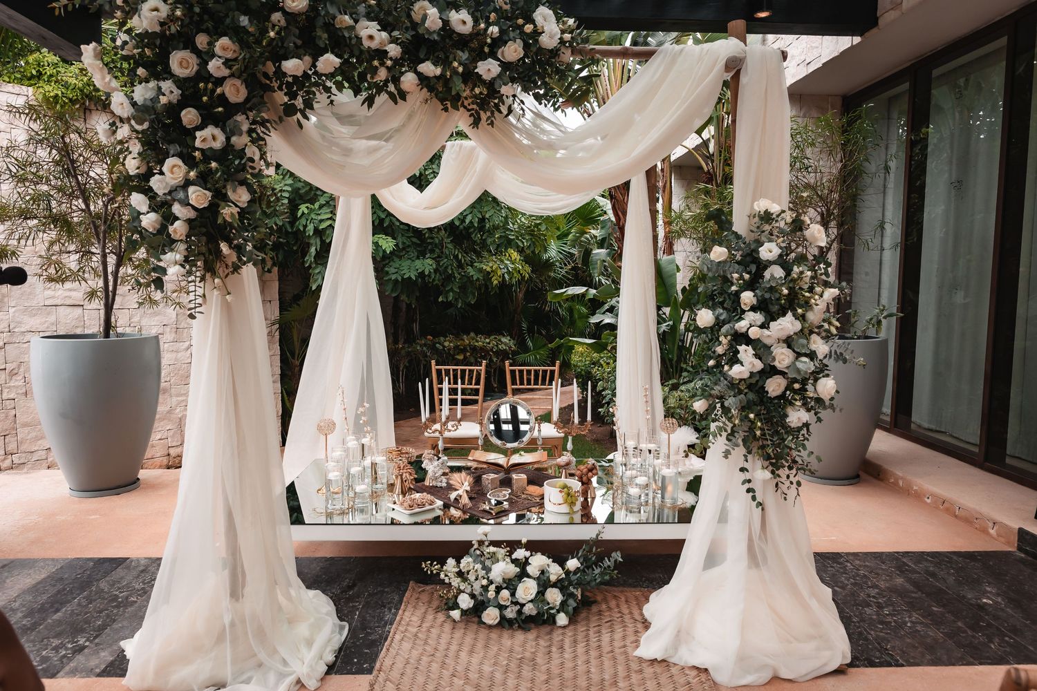 Outdoor wedding venue decorated with white roses and flowing fabric canopies.