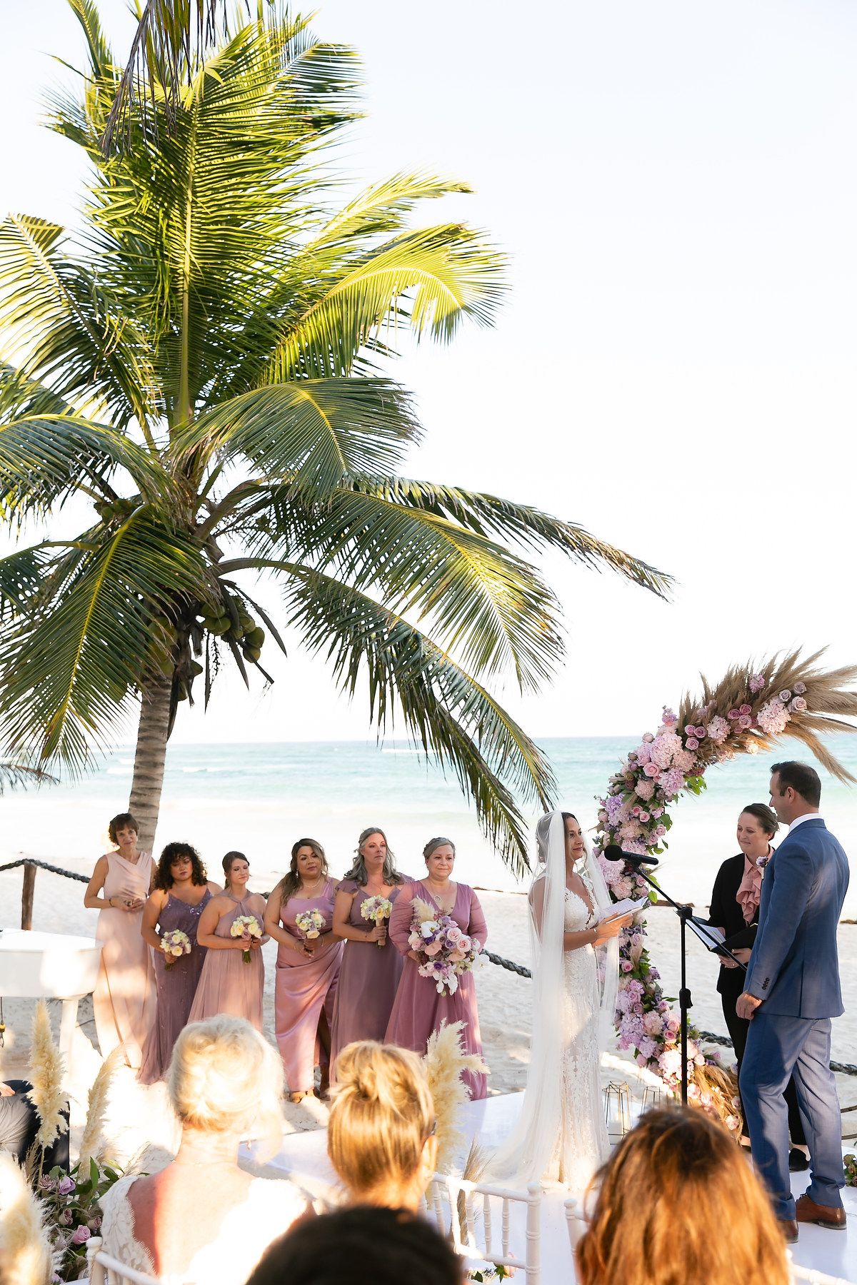 Tropical beach wedding ceremony setup with palm trees swaying in the breeze and white chairs facing the ocean.