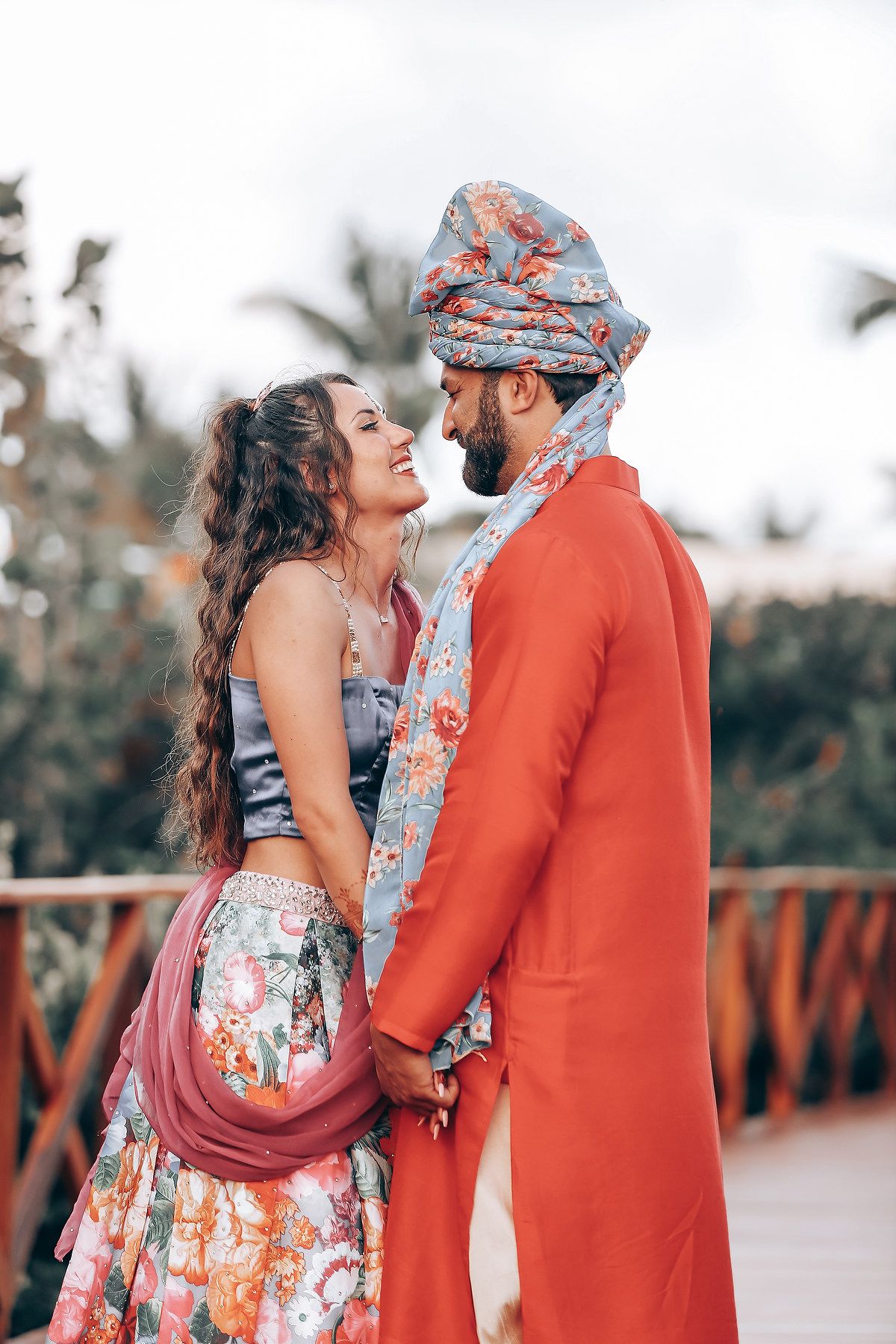 A couple in coordinating floral outfits share an intimate moment on a wooden bridge during sunset.