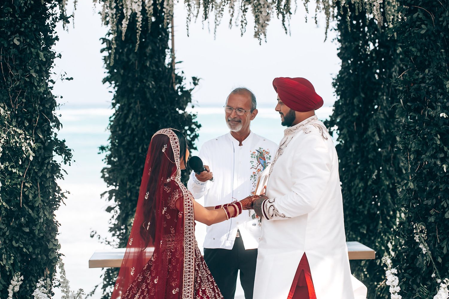Traditional Indian wedding ceremony with bride in red lehenga under floral archway.