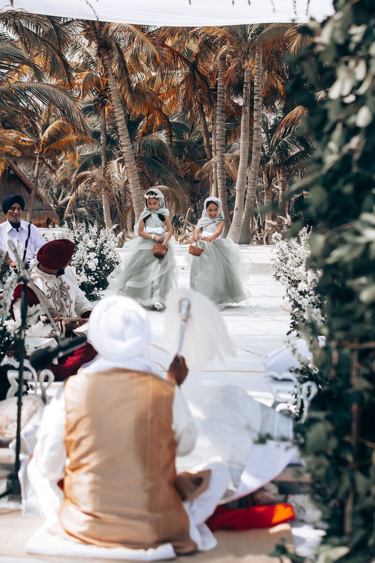 Wedding guests seated on floor during traditional ceremony with tropical palm tree backdrop.