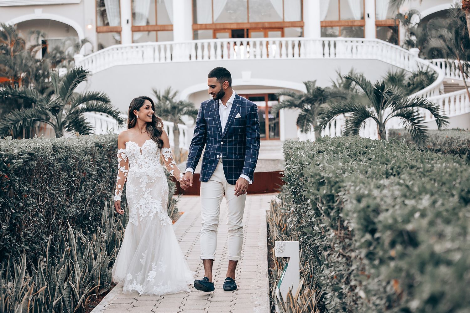 A couple embraces in a romantic garden setting wearing elegant wedding attire.