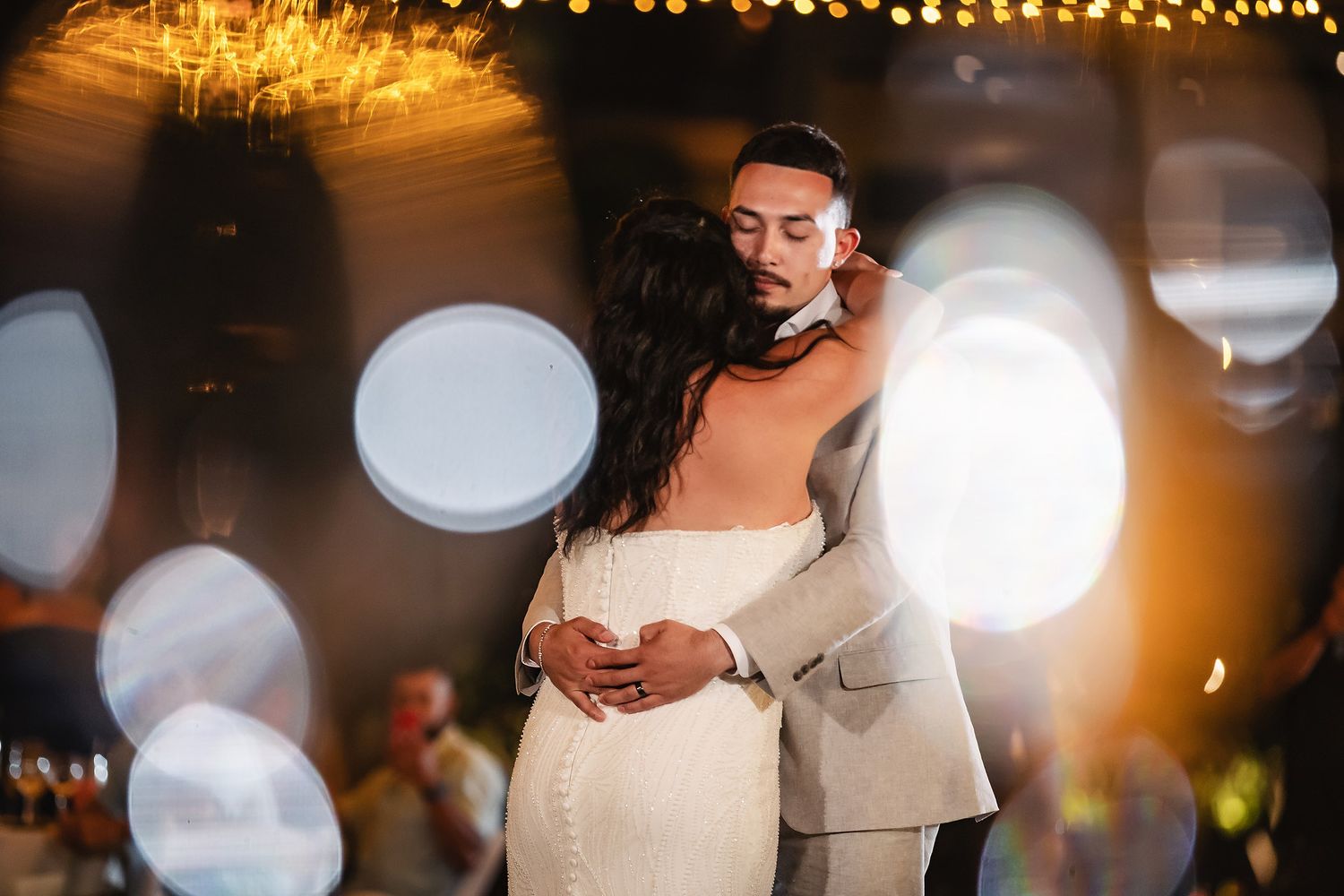 Couple sharing intimate first dance embrace with dreamy bokeh lights at their wedding reception.