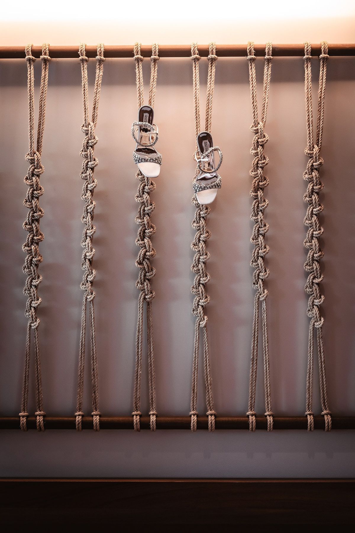 Handcrafted macrame wall hanging with intricate knotted rope patterns displayed on a wooden rod against a neutral background.