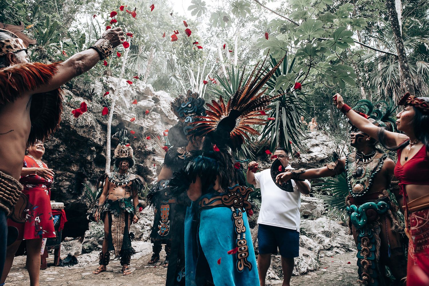 Group of Mayan dancers in traditional feathered costumes perform a ritual ceremony in a jungle setting.