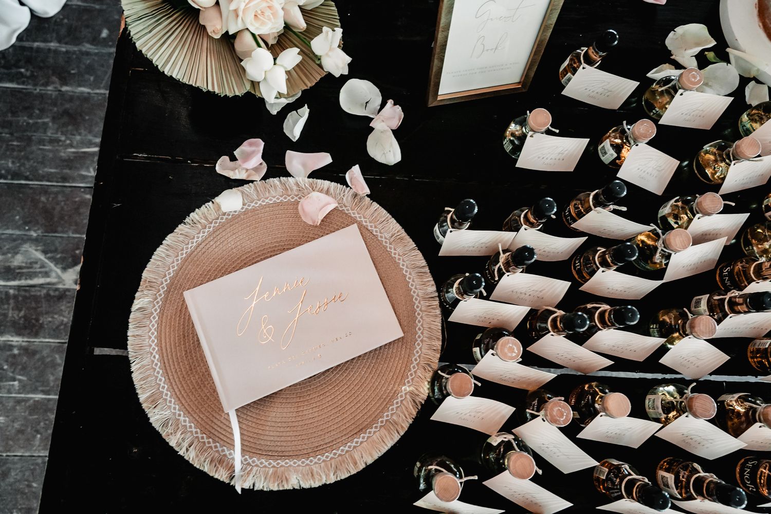 Elegant wedding escort cards display with blush pink plate, floral petals, and rolled paper cones on a dark table.