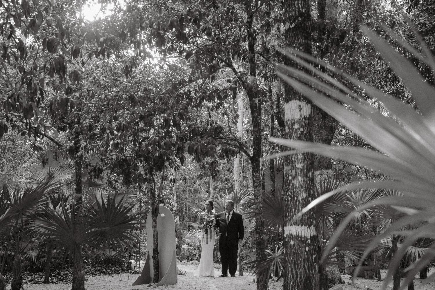 Black and white photo of a couple walking through a lush garden wedding ceremony.