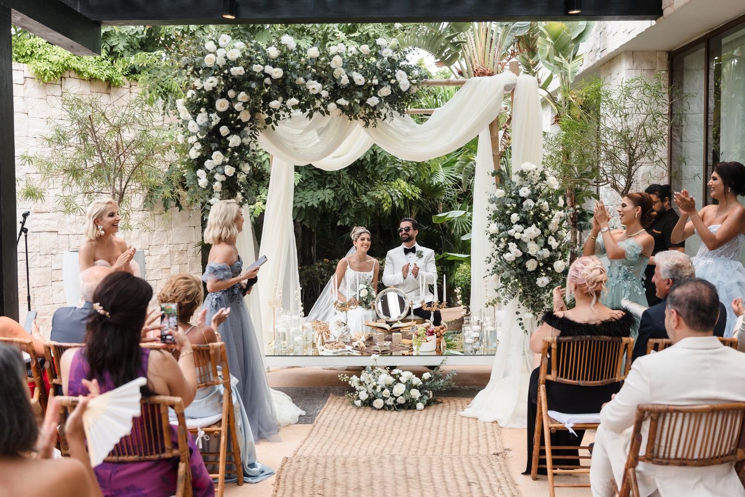 Elegant outdoor wedding ceremony with floral arch, white draping, and guests celebrating the newlyweds.