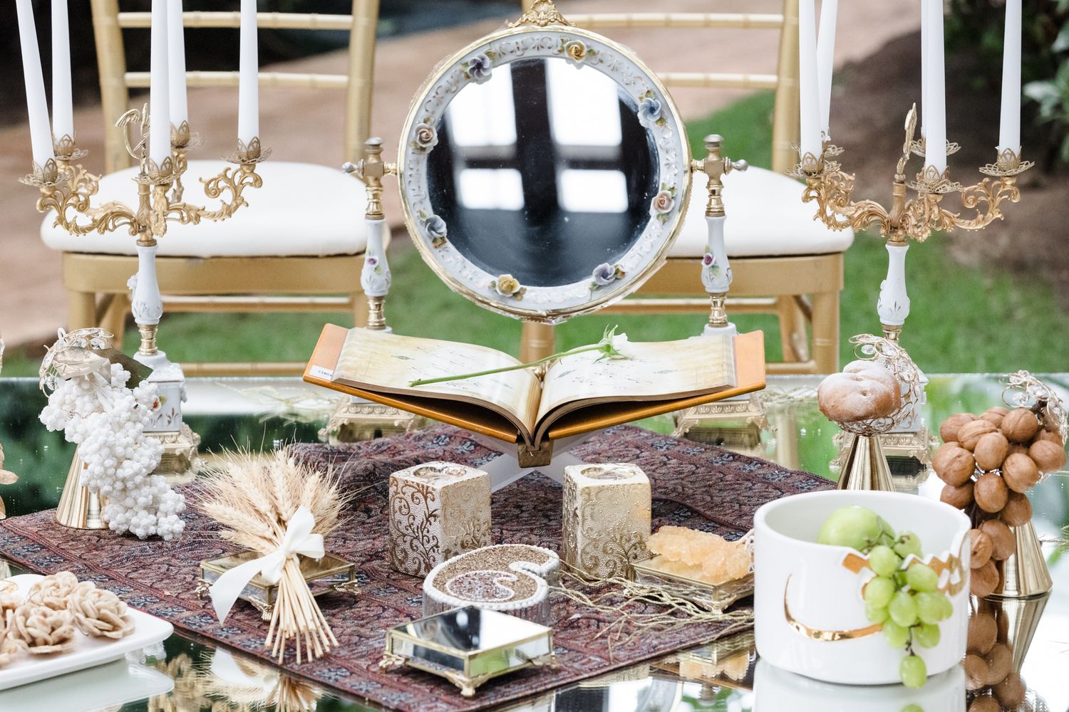 Elegant Persian Sofreh Aghd wedding table with mirror, candles, wheat, and decorative items on ornate rug.