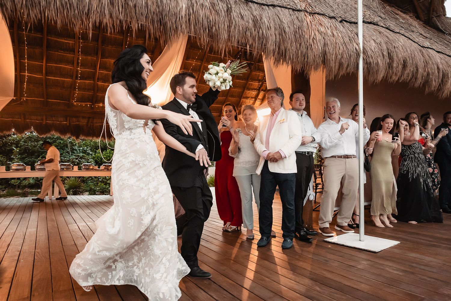 Bride and groom share first dance at tropical wedding reception with guests applauding under thatched roof venue.