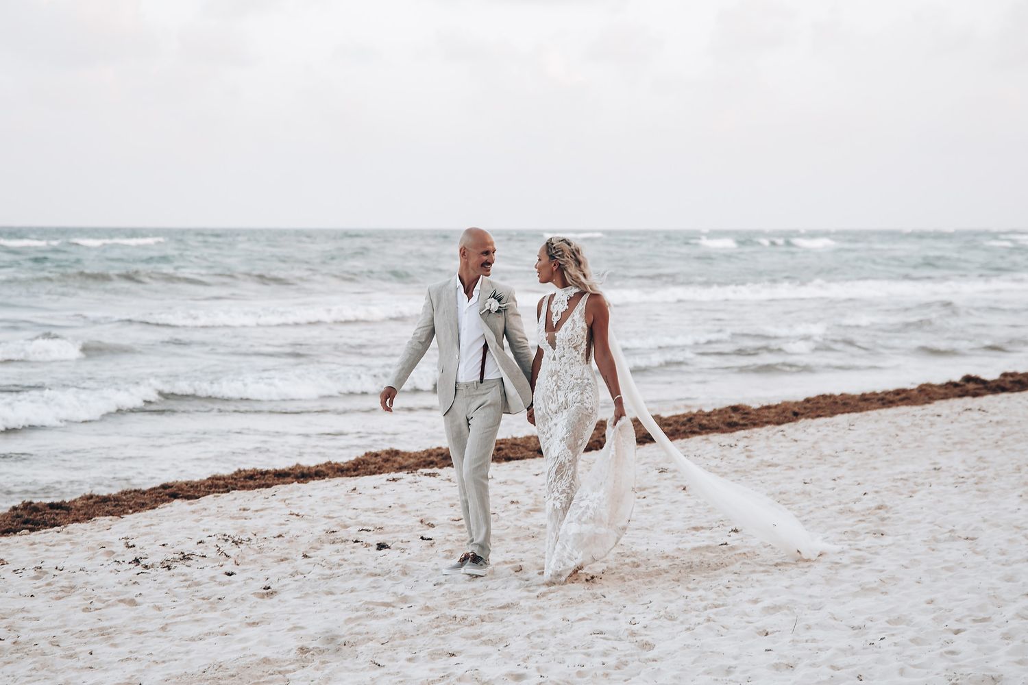Newlyweds walking hand in hand along a serene white sandy beach.