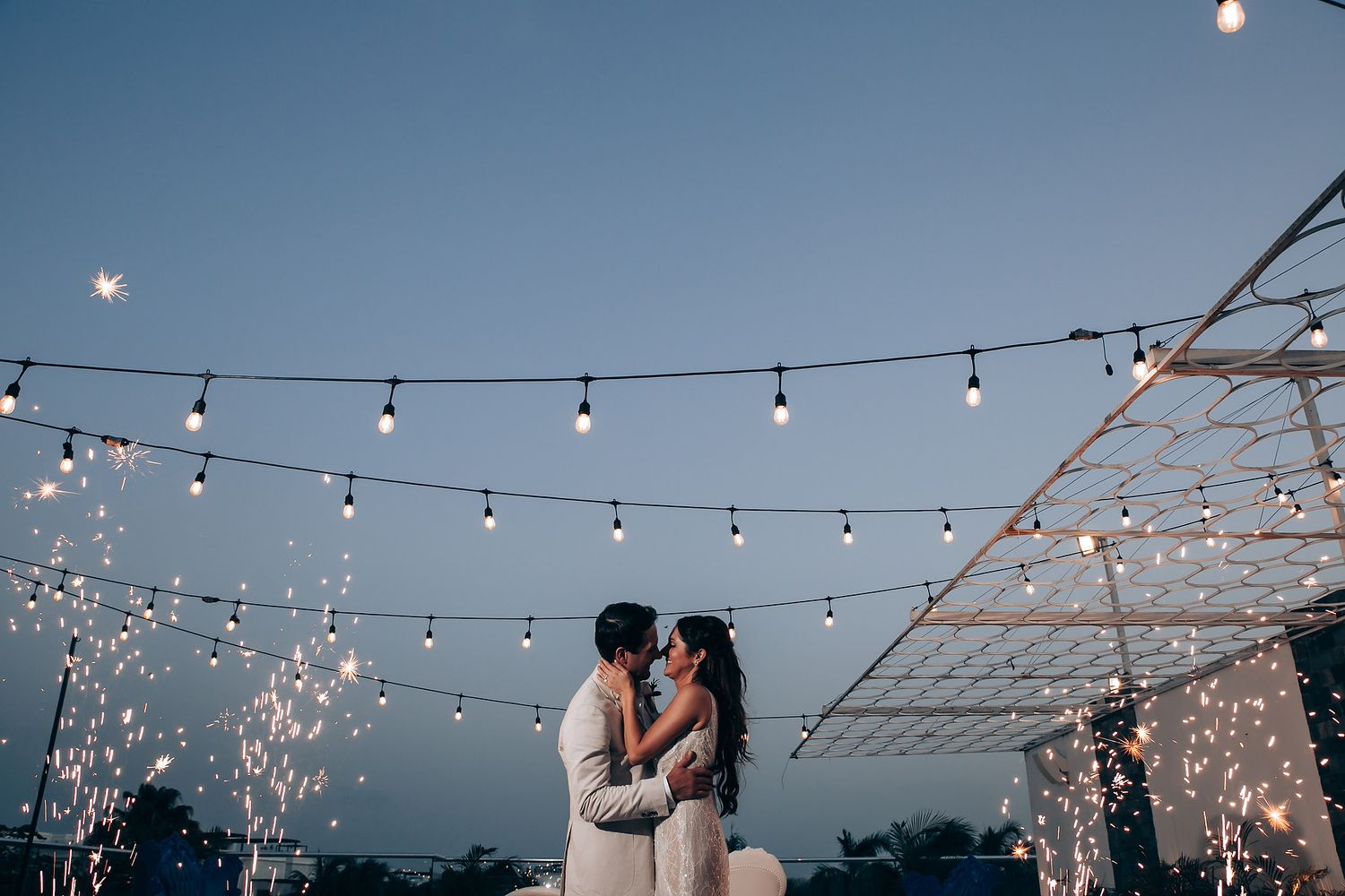String lights illuminate an outdoor evening wedding celebration with sparklers and dancing.