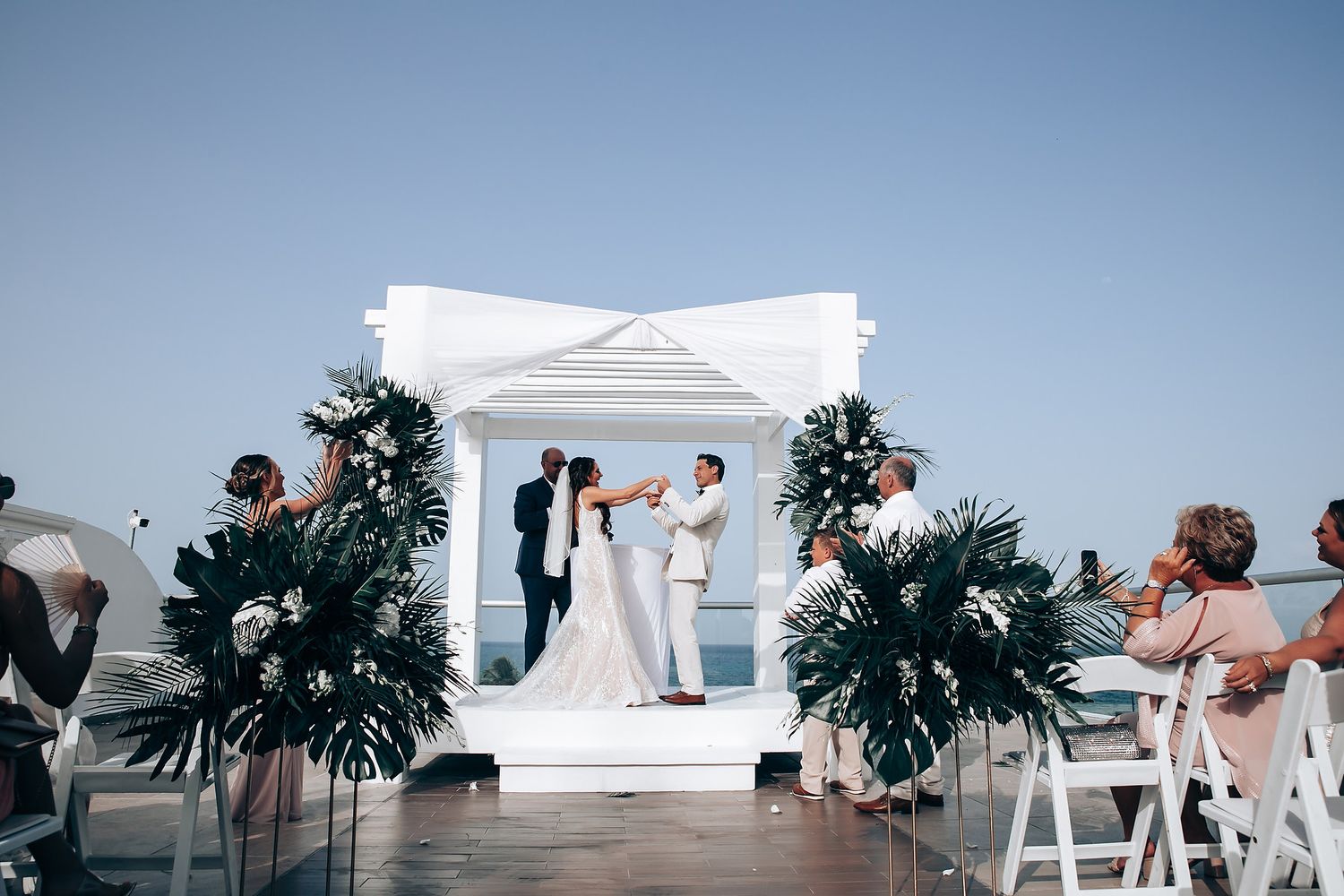 Panoramic wedding scene on a white terrace overlooking the ocean.