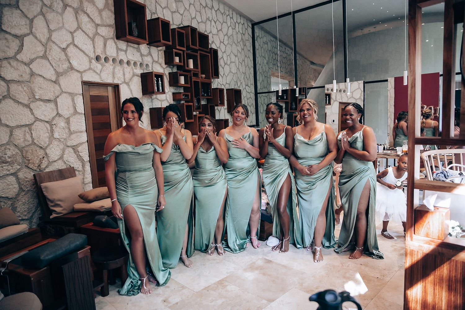 Wedding party members in mint green dresses pose together in an indoor venue.