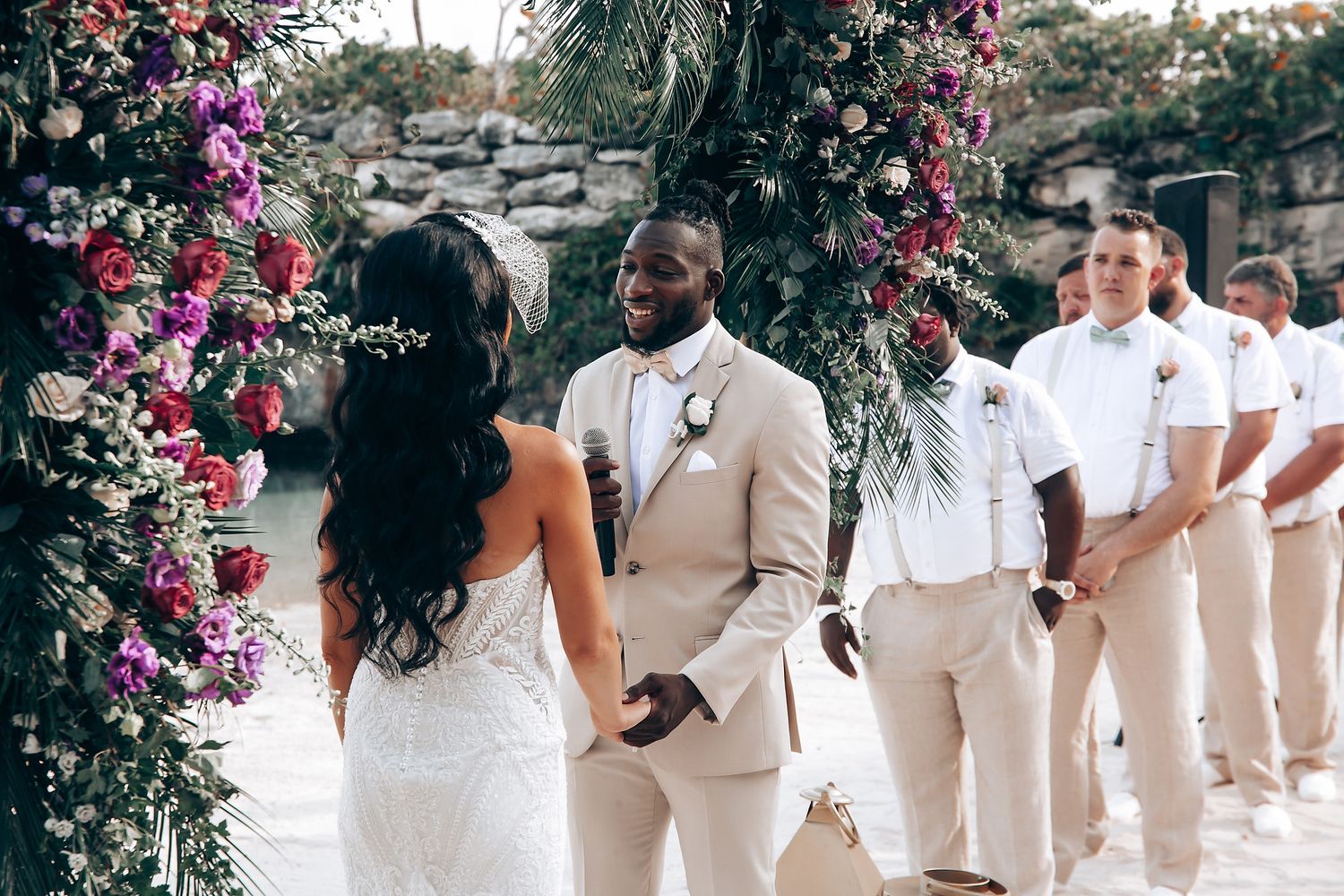Outdoor wedding ceremony with pink floral arch and wedding party in beige attire.