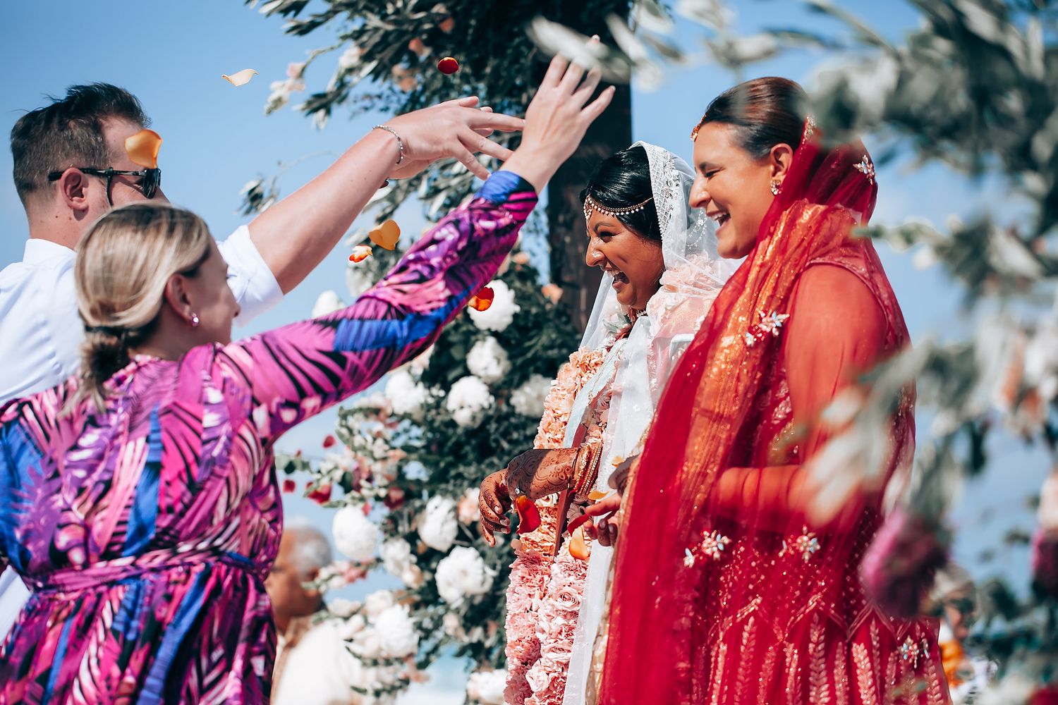 Vibrant outdoor wedding celebration with guests in colorful traditional attire dancing together.