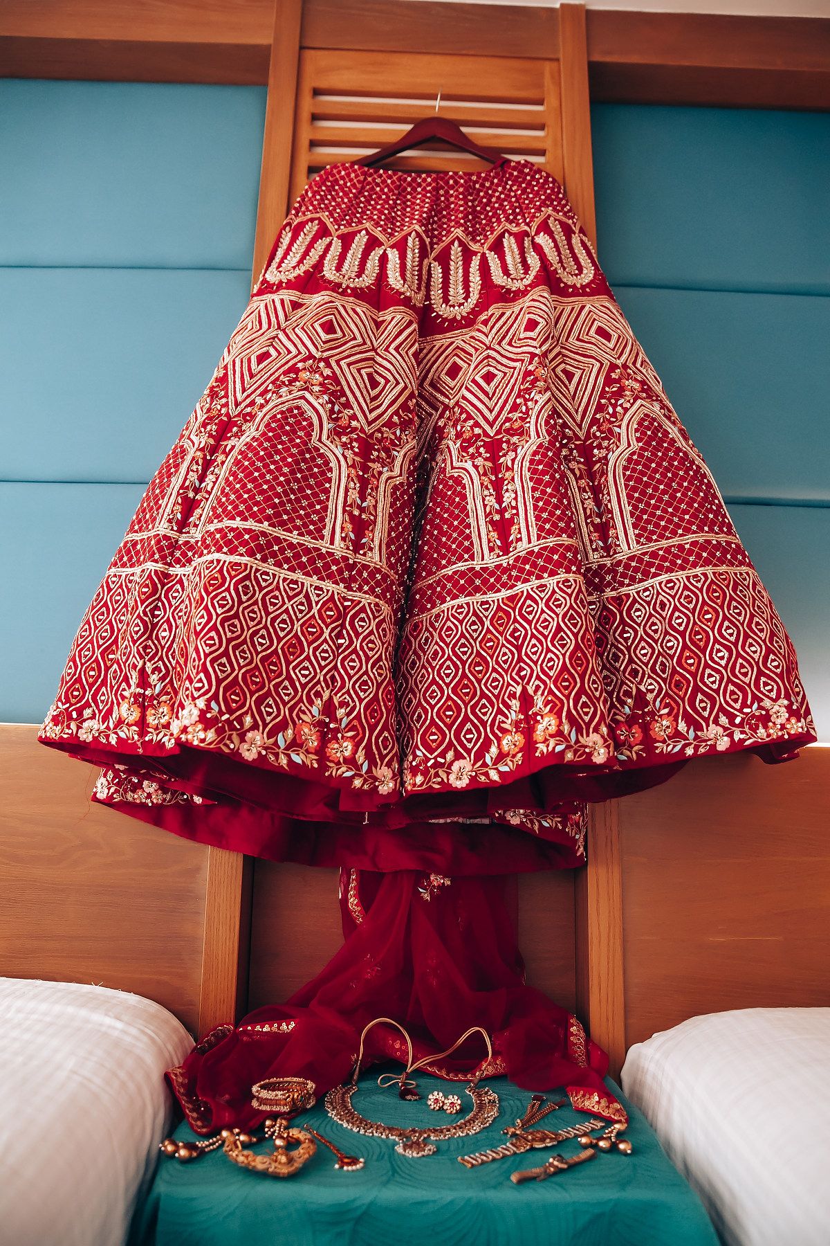 Ornate red and white traditional Indian lehenga skirt hanging with jewelry displayed below.