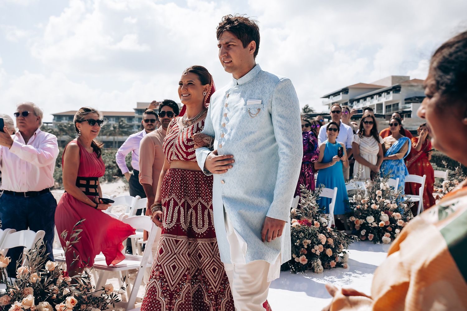 Wedding celebration on a sunny beach with guests in formal attire.