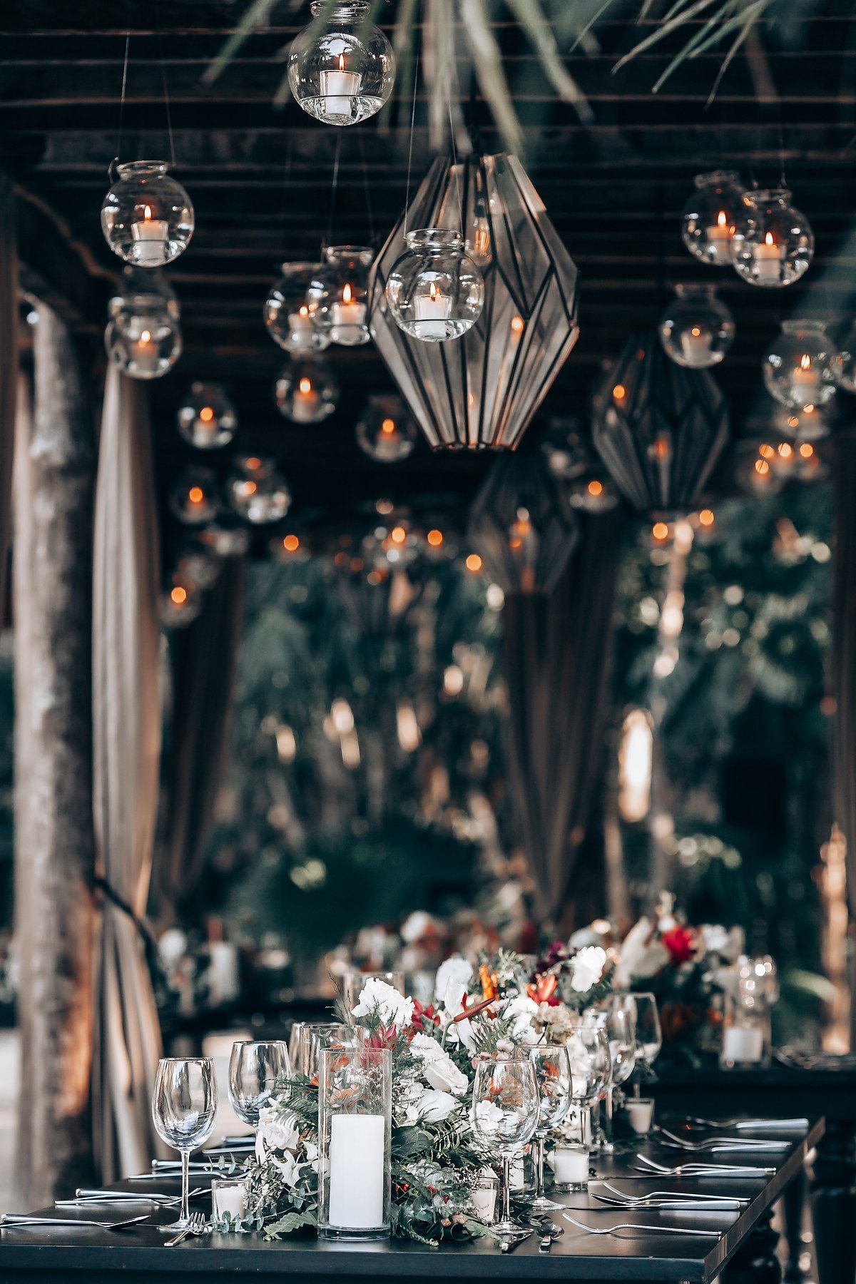 Elegant wedding reception table setting with hanging geometric light fixtures and moody dark ambiance.