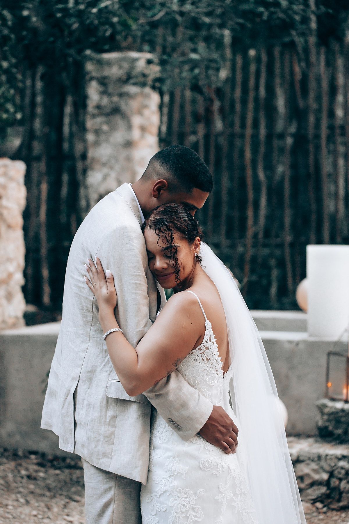 A couple in wedding attire sharing an intimate moment outdoors in a wooded setting.
