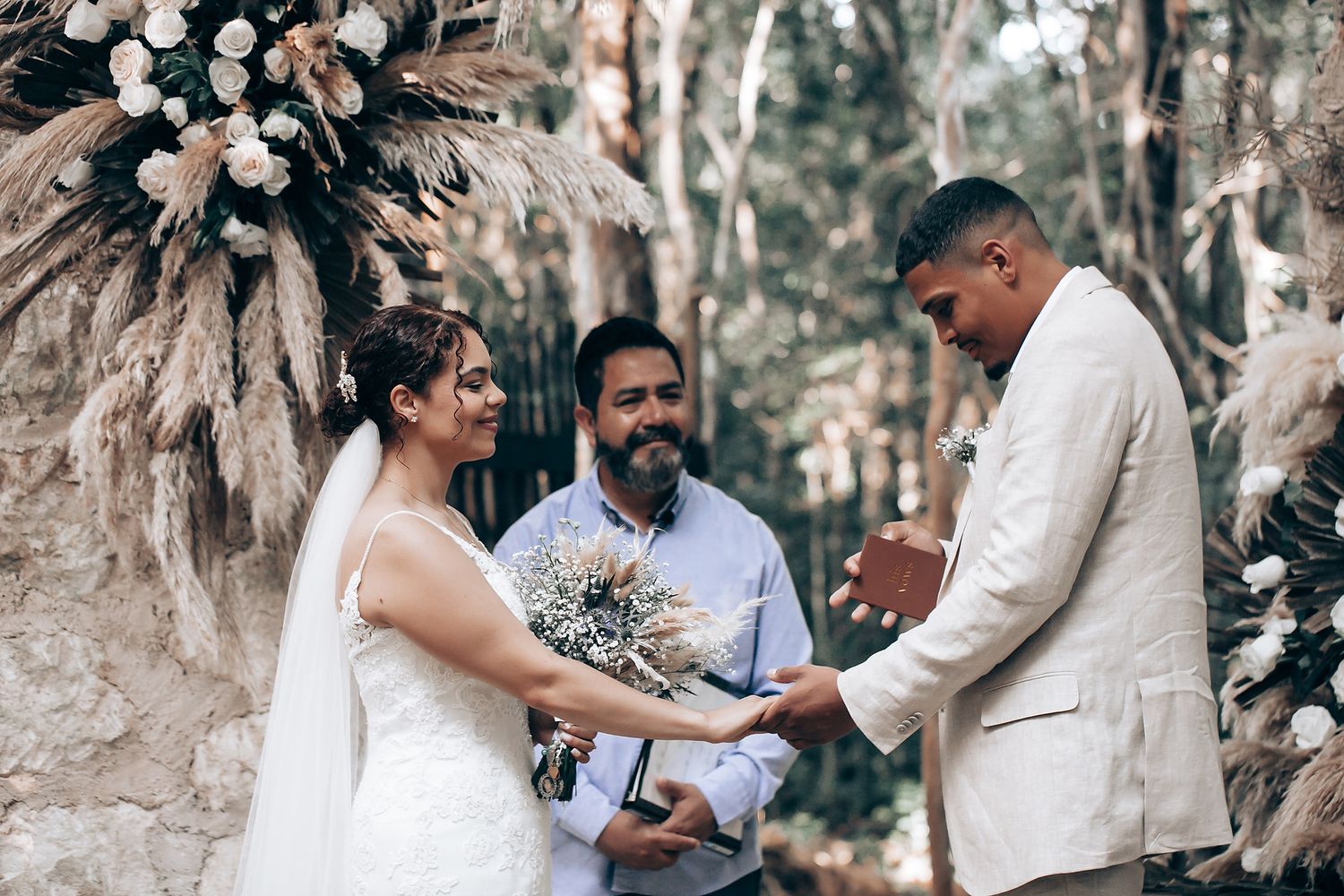 Wedding celebration in progress among trees with decorative floral arrangements.