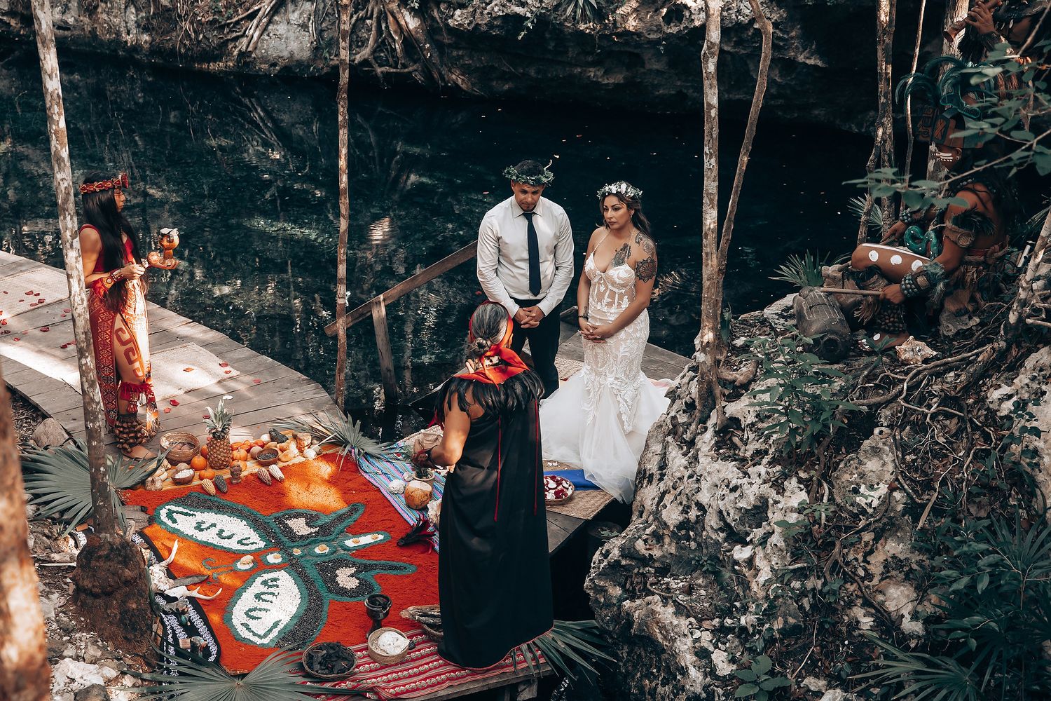 Guests witness a beautiful ceremony in a naturally lit cave with stone walls and scattered flowers.